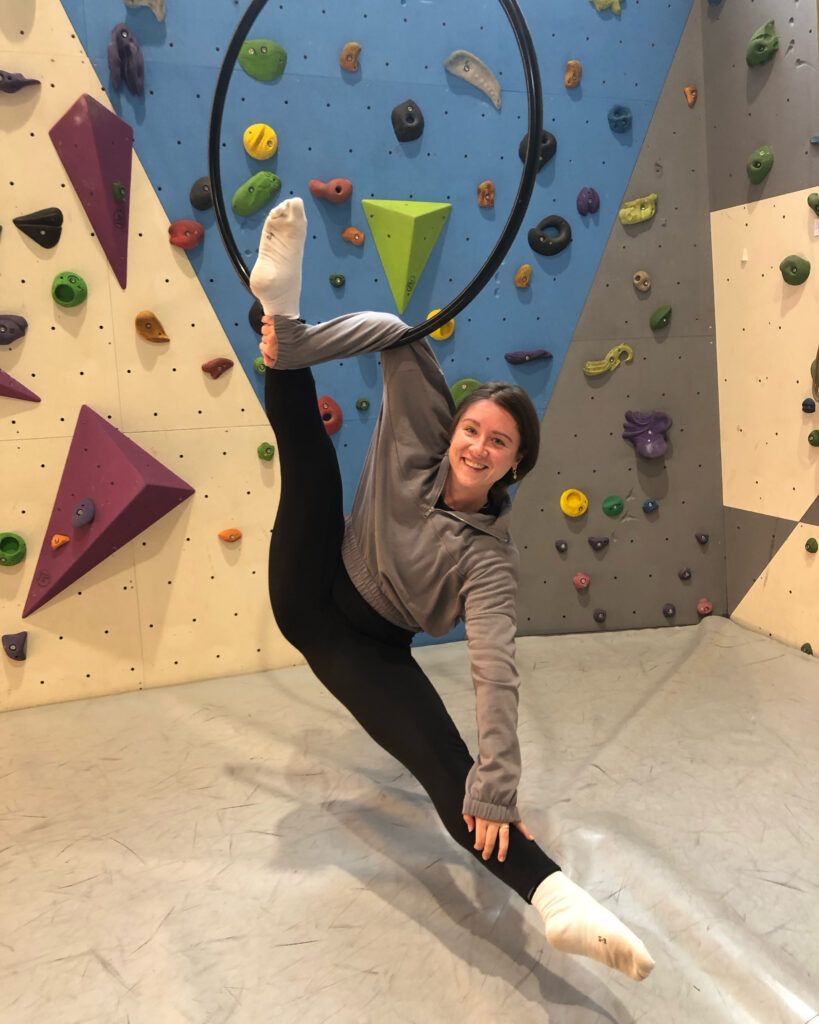 Sarah-Nikita Kröger lächelt im Aerial Hoop vor einer Kletterwand